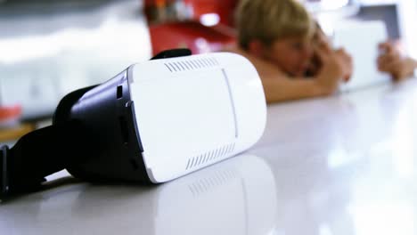 Close-up-of-virtual-reality-headset-on-kitchen-worktop-while-siblings-using-digital-tablet