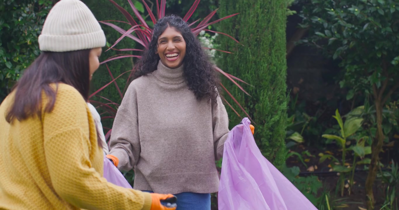 Voluntarias africanas abriendo una bolsa morada, recogiendo una botella de plástico durante la limpieza de un jardín.