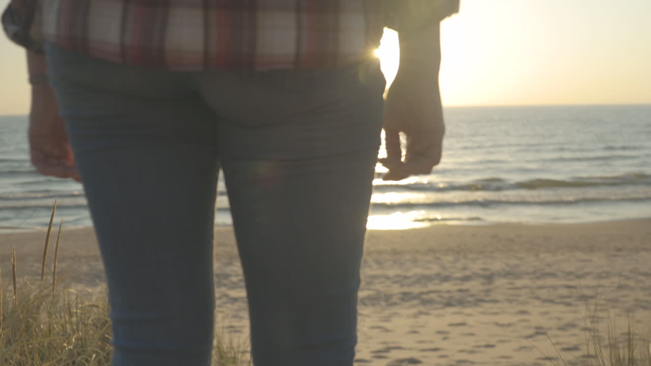 Handheld shot of a young woman walking down a sandy path toward a beach at sunset.  Shot in 4K