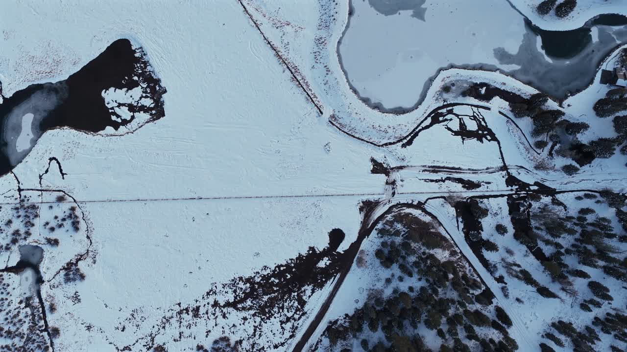 Unique top-down shot of a frozen pond and wide snowy field. The scene captures the stunning abstract patterns and unique textures of the ice and snow terrain at Wolf Creek, Colorado