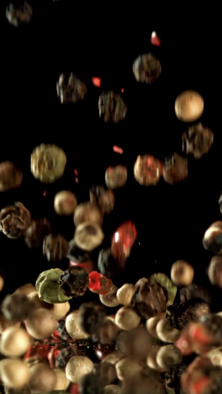 Mixed Peppercorns Falling and Bouncing on a Reflective Black Surface in Slow Motion