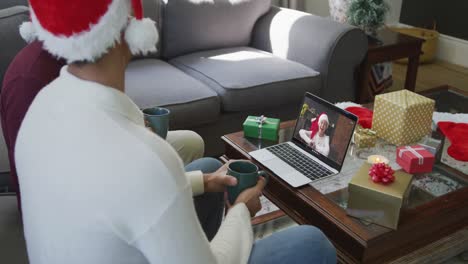 Padre-E-Hijo-Birraciales-Usando-Una-Computadora-Portátil-Para-Una-Videollamada-Navideña-Con-Una-Mujer-Sonriente-En-La-Pantalla