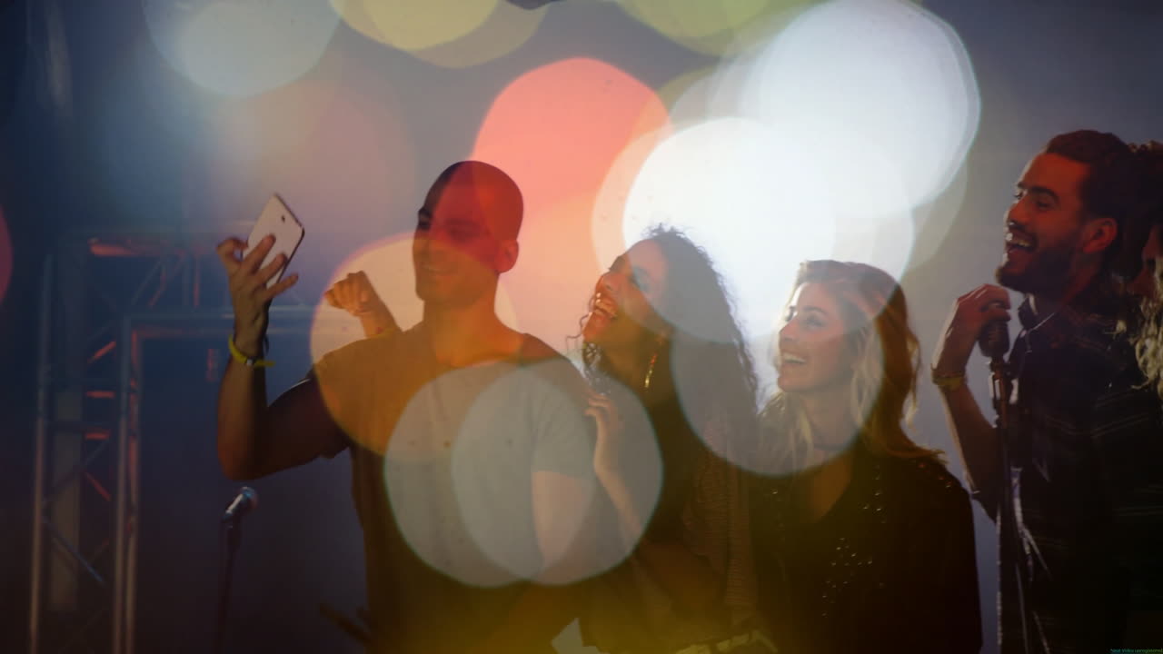 Music team taking smartphone selfie on stage, with animated notes floating above microphones
