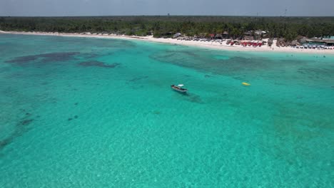 Boat-anchor-off-tropical-beach-in-clear-blue-ocean-water-with-trees-in-background--aerial-pull-back