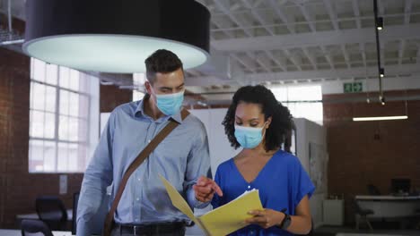 Diverse-race-male-and-female-businessmen-walking-discussing-through-corridor-wearing-facemask