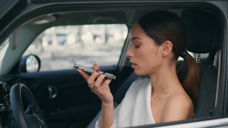 una mujer de negocios usando la función de reconocimiento de voz de un teléfono inteligente sentada en un coche de cerca.
