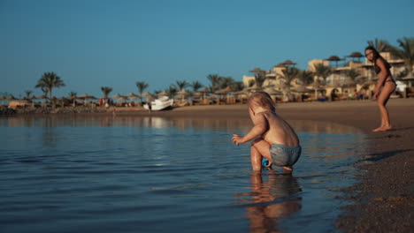 little quiet baby boy walking to seawater at sunrise beach in hurghada resort.