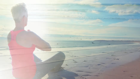 animation of glowing light over senior woman practicing yoga by seaside