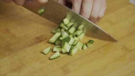 chef cuts cucumbers with kitchen knife on wooden cut board