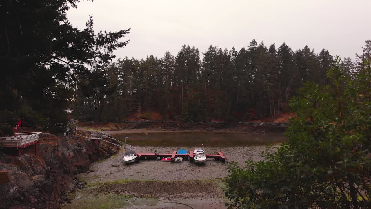 Drone 4K Footage of a boat launching dock at low tide exposing boats on land with a forest along the coasts