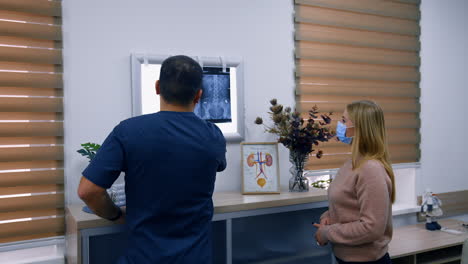 patient and doctor standing in the hospital cabinet. medic explaining the x-ray scan hanging on the light screen.