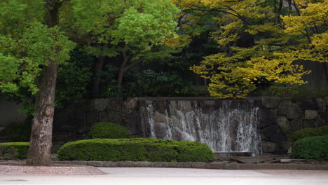 a small artificial waterfall surrounded by vegetation in peaceful ueno park, tokyo