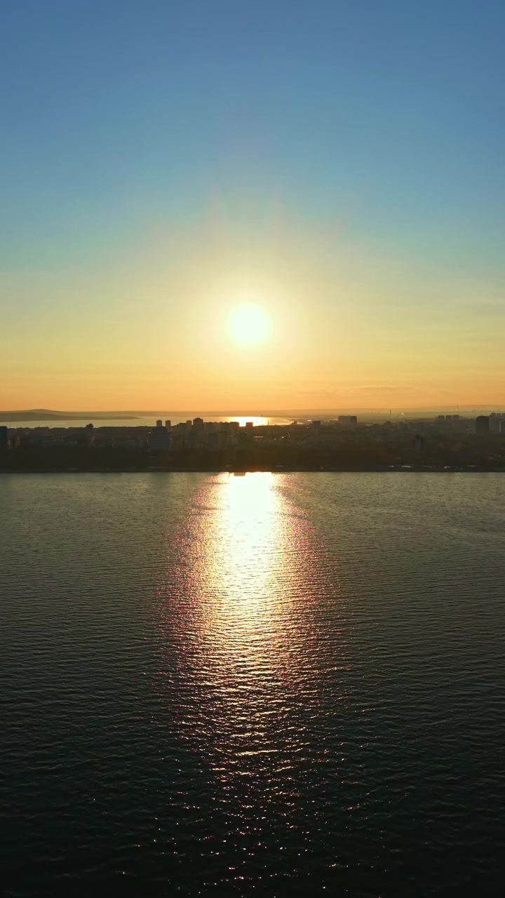 Sunrise over the water with city skyline in the background at dawn in a coastal area, showing the first light of the day reflecting on the surface