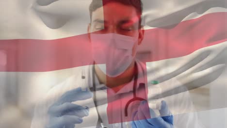 Animación-De-La-Bandera-De-Inglaterra-Ondeando-Sobre-Un-Médico-Con-Mascarilla-Y-Sosteniendo-La-Vacuna