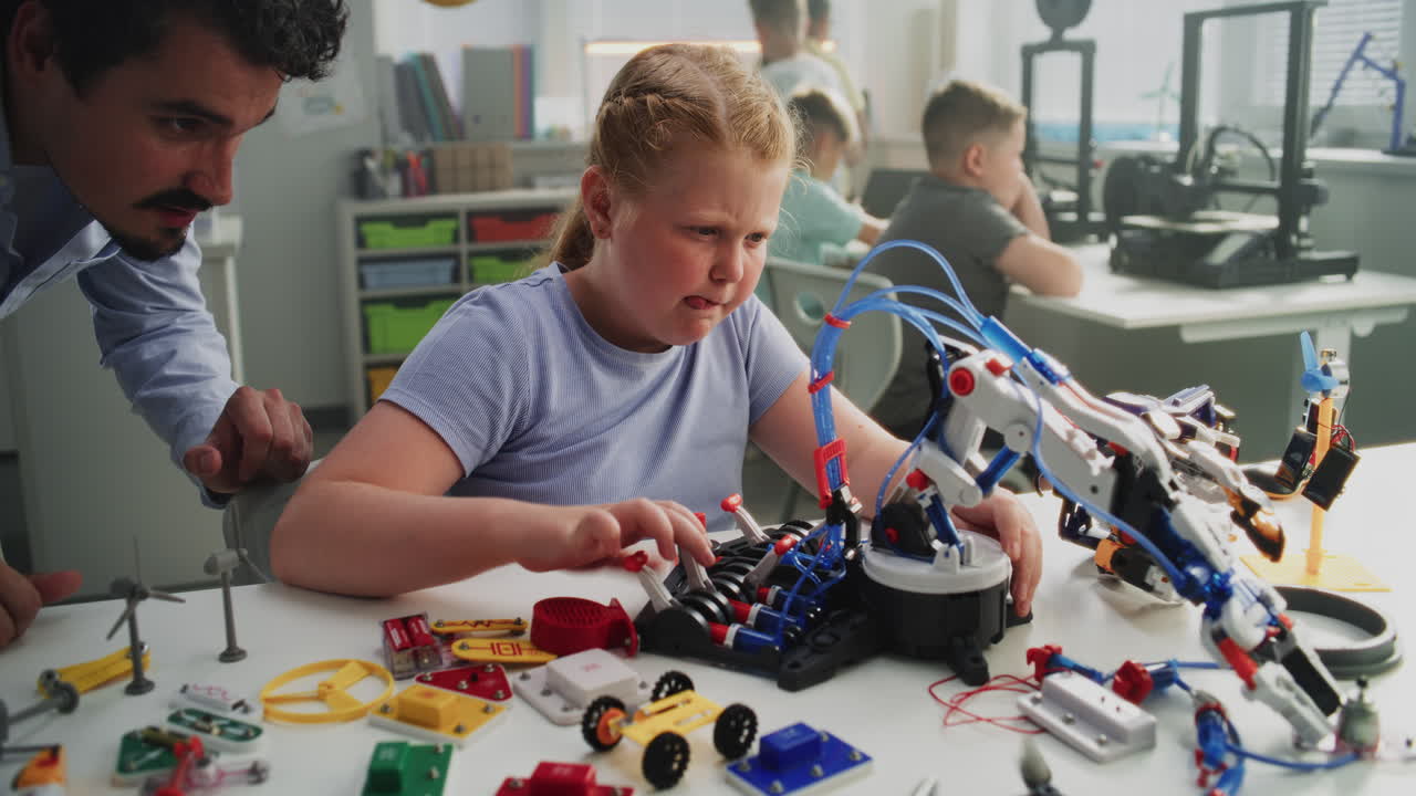 Talented Young Girl Sitting at the Desk Studying Robotic Arm Model with Male Teacher