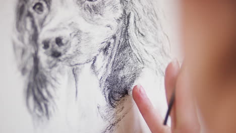 primer plano del artista sentado en el caballete dibujando una imagen de perro en carbón