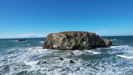 beautiful 4k aerial drone shot with blue skies gliding over bandon beach towards giant rock on a sunny day