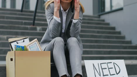 close-up view of caucasian young woman sitting on stairs at street with 
eed work" signboard and box with stuff"