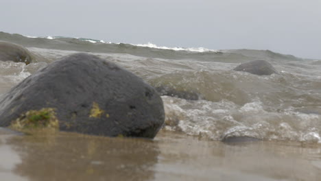 Blick-Auf-Das-Wasser,-Das-Sich-Zwischen-Steinen-Am-Sandstrand-Der-Insel-Gran-Canaria-In-Spanien-Bewegt