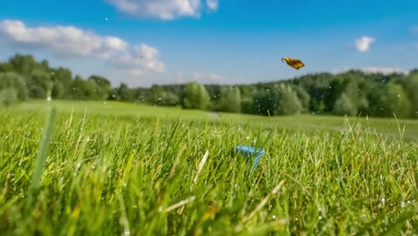 Der-Golfschläger-Schlägt-In-Superzeitlupe-Auf-Einen-Golfball.-Nach-Dem-Aufprall-Steigen-Morgentautropfen-Und-Graspartikel-In-Die-Luft.