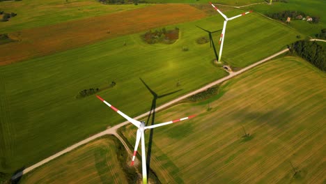 drone shot of the wind turbines working in a wind farm generating green electric energy on a wide green field on a sunny day, in the background there is solar panels plant