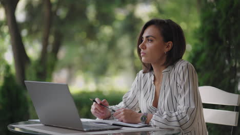 talented serious woman brunette hispanic ethnic group sits at a table in a summer cafe with a laptop. considers solving problems. puzzled business woman. portrait of a beautiful business woman