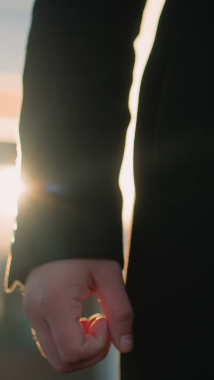 반이는 금속 버튼을 입은 검은 옷을 입은 남자가 밖에서 서서 빛이 그의 오른손에서 반사되는 것처럼 조화로운 표정을 지니고 있으며, 전문성을 발휘하고 있으며, 배경에는 현대적인 유리 건물이 있습니다.