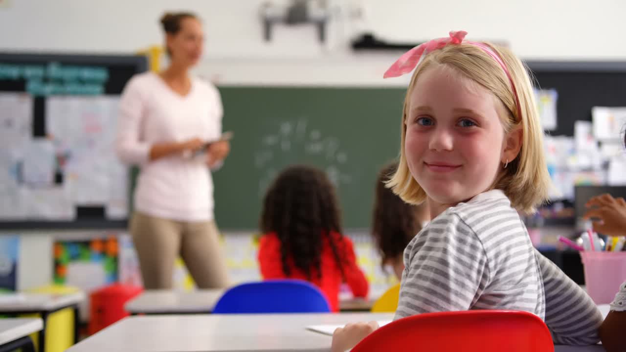 Achteraanzicht van blij Kaukasisch schoolmeisje dat in de camera kijkt in het klaslokaal 4K