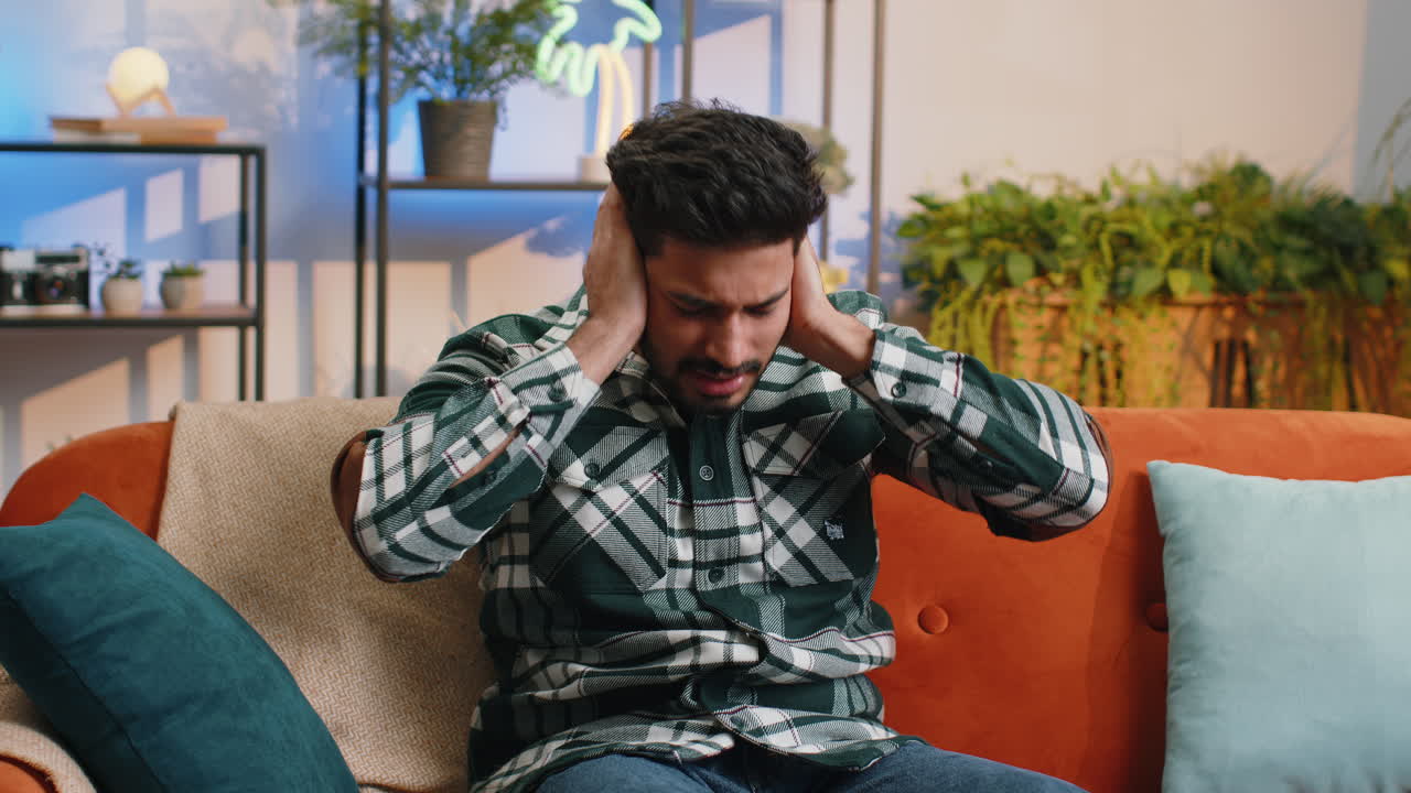 Repair work at neighbours concept irritated man at home cover ears with pillows annoyed by noise