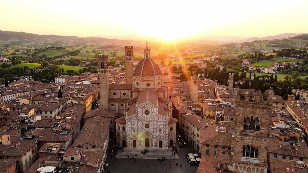Vista aerea mozzafiato di una città storica al tramonto, con una maestosa cattedrale circondata da affascinanti tetti e lussureggianti colline verdi sullo sfondo.