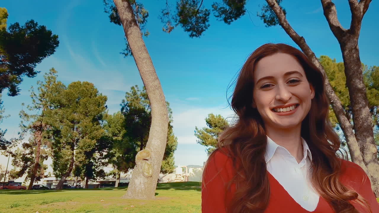 A happy, attractive, young, caucasian woman at the park, turns her head to the camera and lets out a big smile