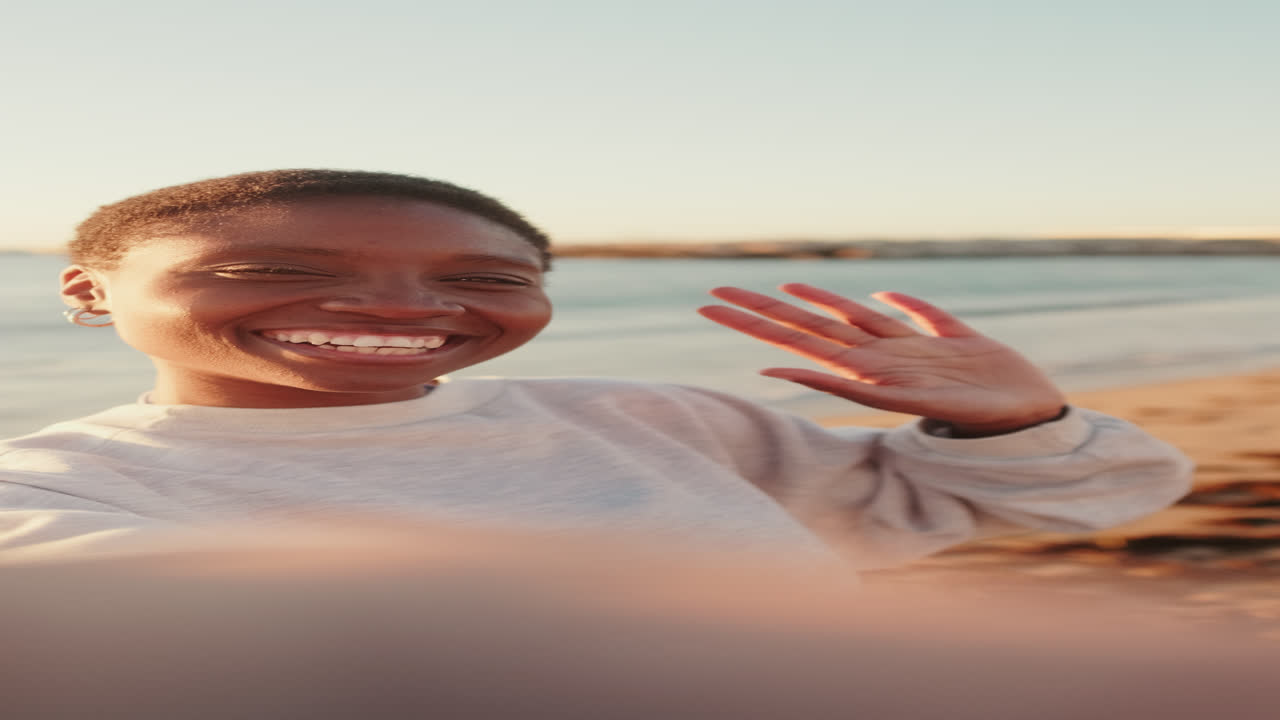 Iloinen afroamerikkalainen nainen ottaa selfie-videota rannalla auringonlaskun aikaan