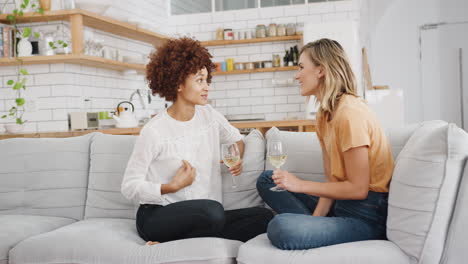 dos amigas relajándose en el sofá en casa con un vaso de vino hablando juntas