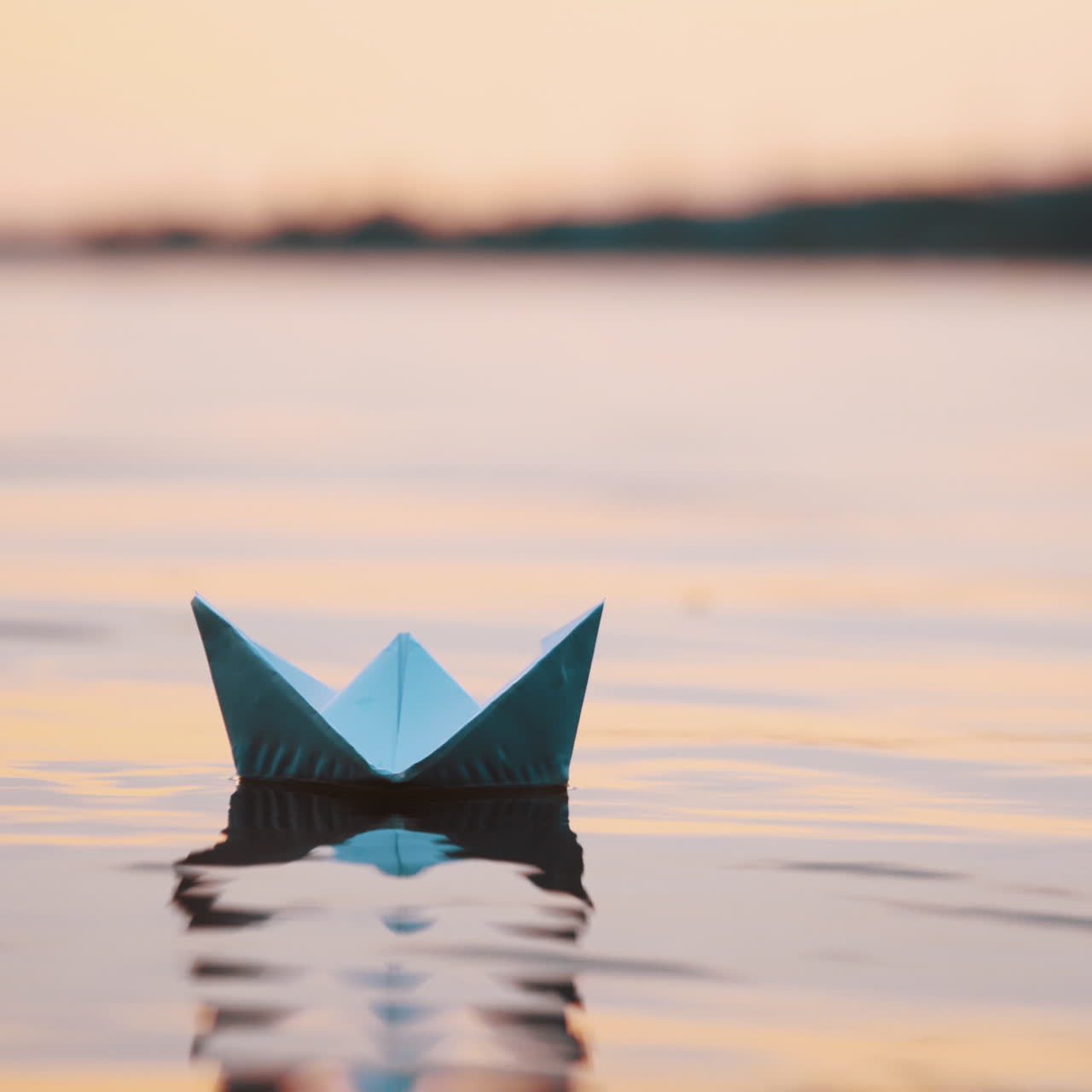 Nice paper boat on evening water surface. One blue origami ship sailing in the river calmly with its reflection outdoors.