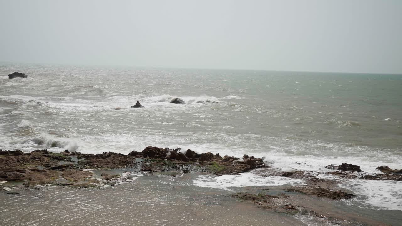 Waves crash on a rocky shoreline under an overcast sky, creating a peaceful coastal scene