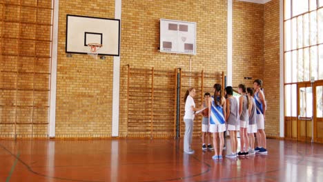 female coach instructing school students in basketball court