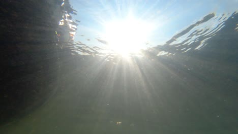 una vista mirando hacia arriba desde el fondo del lecho de un río mientras el sol y sus rayos brillan en el agua