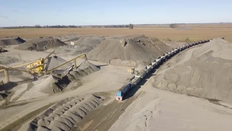 a busy quarry in argentina with heavy machinery, train being loaded and long conveyor belts, aerial view