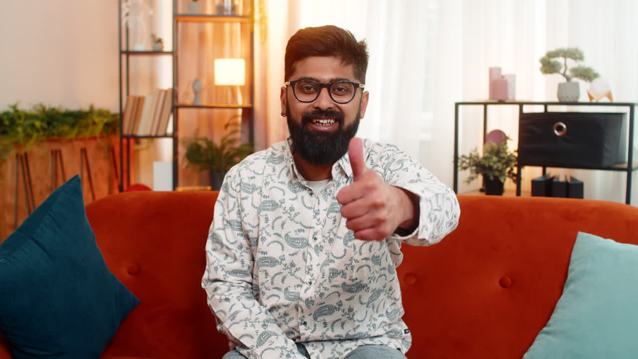 Indian man showing thumbs up with satisfied expression positive gesture of approval relaxing at home