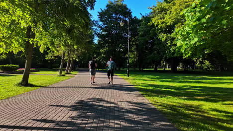 two men with backpacks walking in a shady park with fresh air in the morning in liepaja, latvia