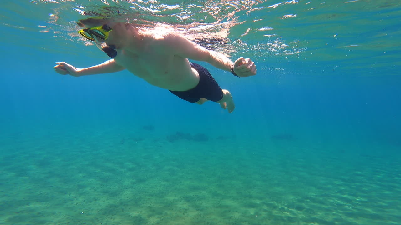 Un giovane subacqueo nuota in superficie nel Mediterraneo, vicino a una spiaggia su un'isola greca, con vista subacquea.