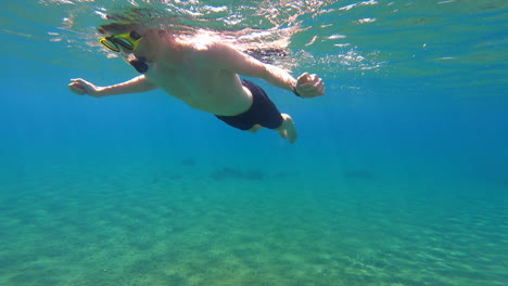 A-young-scuba-diver-swims-on-the-surface-of-the-Mediterranean,-near-a-beach-on-a-Greek-island,-underwater-view