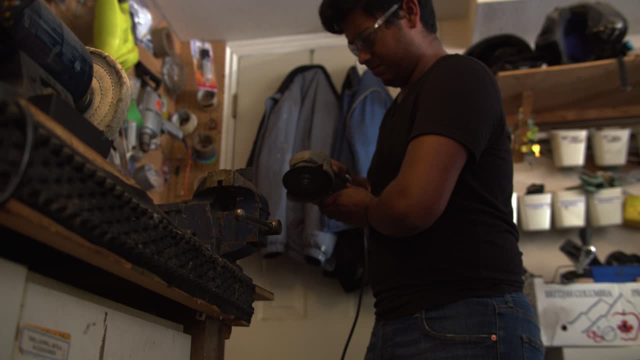 adolescente asiático que trabaja en el garaje dando forma al metal en la amoladora de banco, encendiendo chispas en 4k