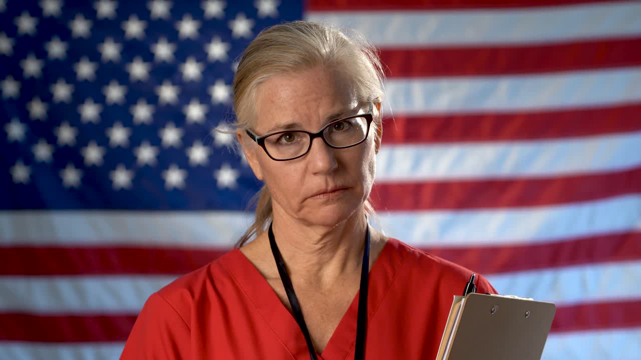 Portrait of a nurse walking from US flag to foreground and showing an extreme sadness and disapproval