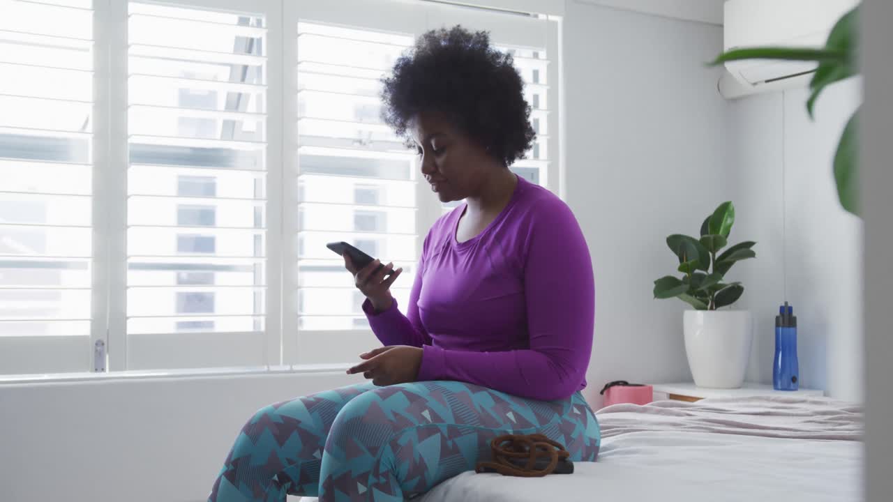 African american female plus size sitting on bed using smartphone