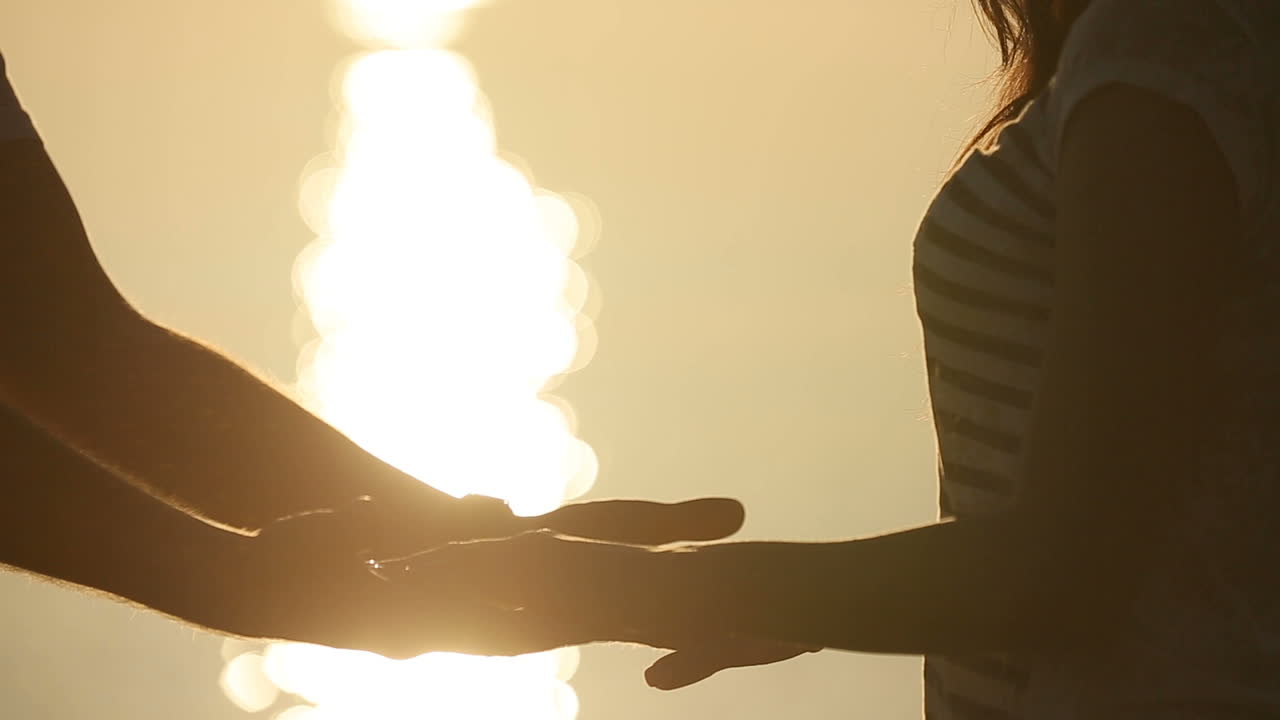 Hands couple against sunset. Close up of silhouette couple holding by the hands near pond