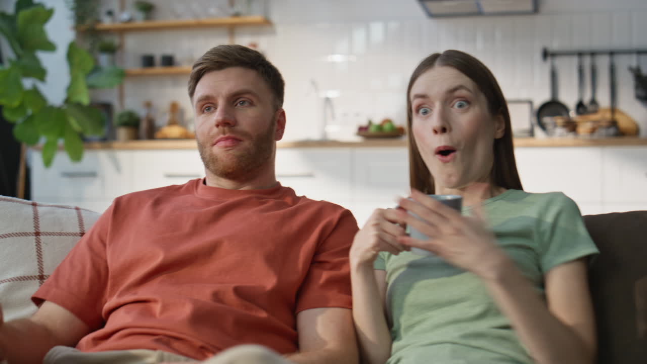 Cặp đôi gia đình cùng nhau xem TV trên ghế sofa tại nhà cận cảnh. Người vợ và chồng đầy cảm xúc