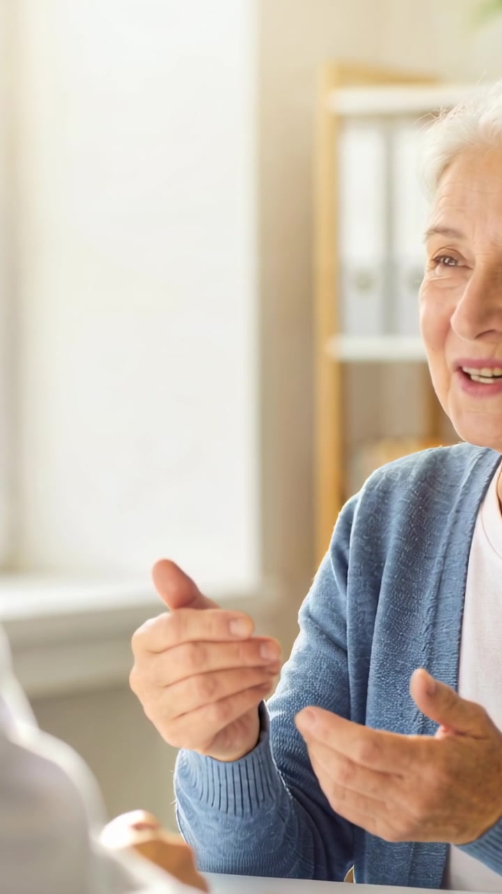 Video verticale: Donna anziana in cardigan blu che parla e risponde al partner in clinica, con dei raccoglitori.