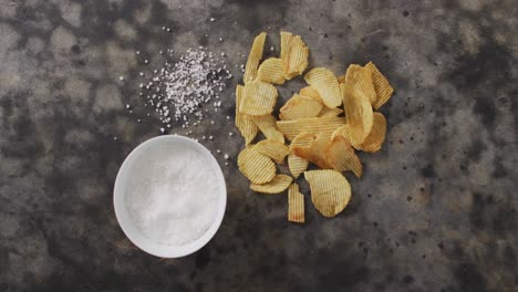 close up of potato chips and bowl of salt on black surface