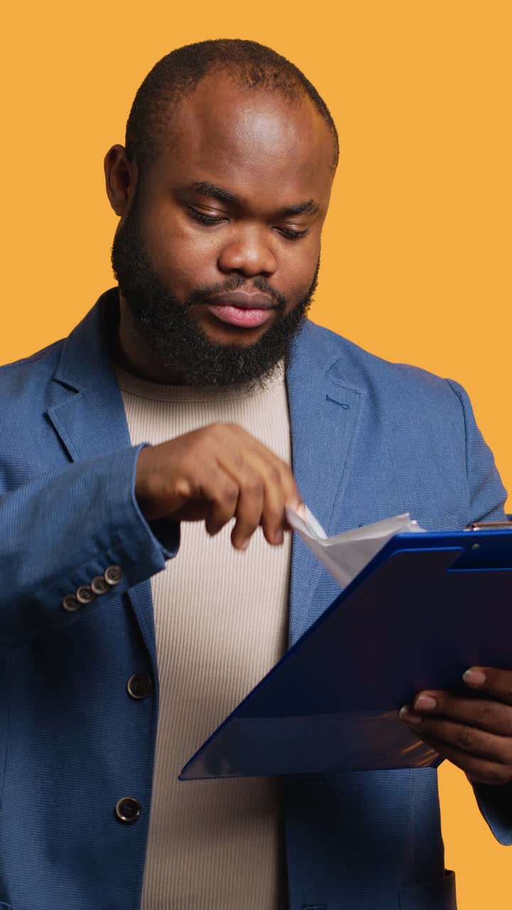 Vertical video Man browsing though financial audit report on clipboard, yawning, feeling tired